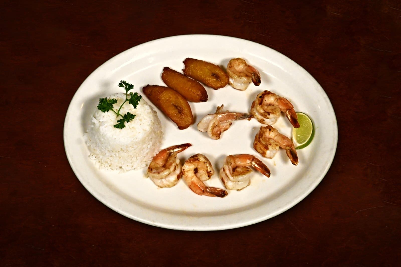 Camarones a la Plancha: marinated & grilled, white rice, maduros, plated on a dark wood table