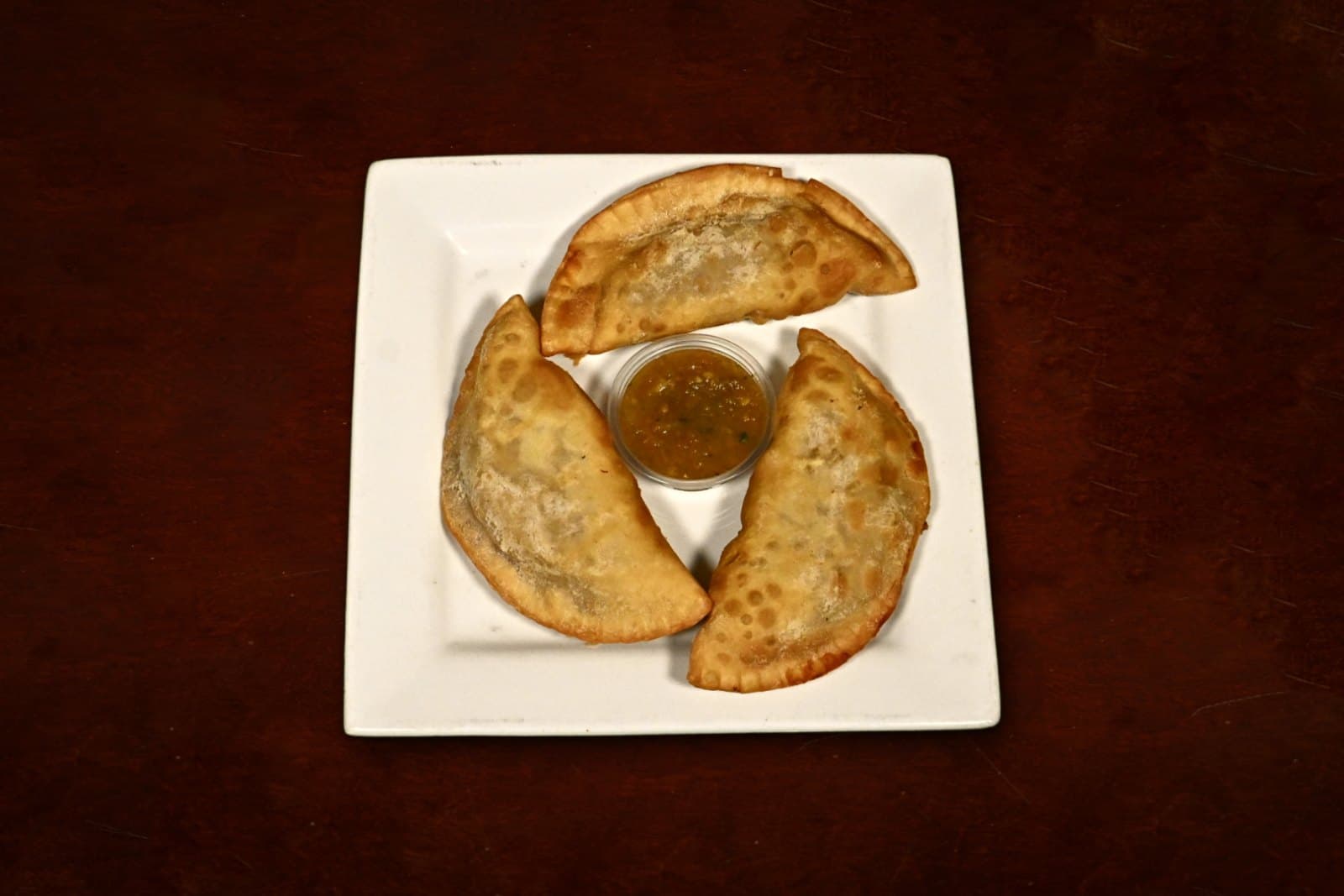 Empanadas: three per order, golden & crisp, plated on a dark wood table