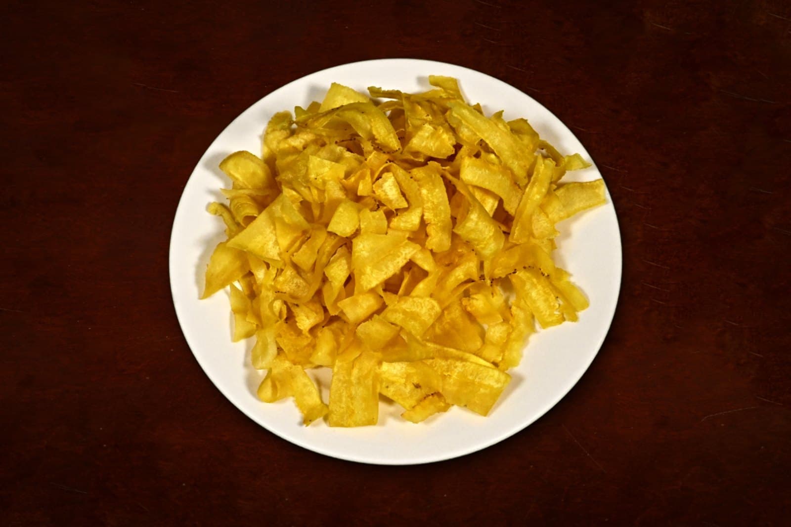 Mariquitas: thin-sliced green plantains, fried crisp, plated on a dark wood table