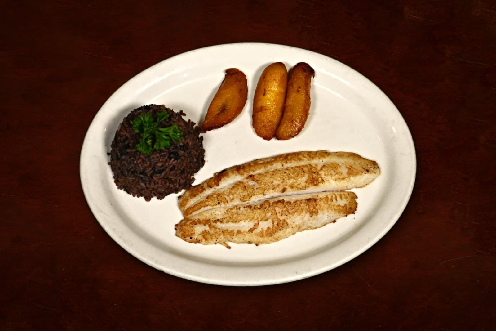Filete de Pescado: marinated & grilled, moros, maduros, plated on a dark wood table