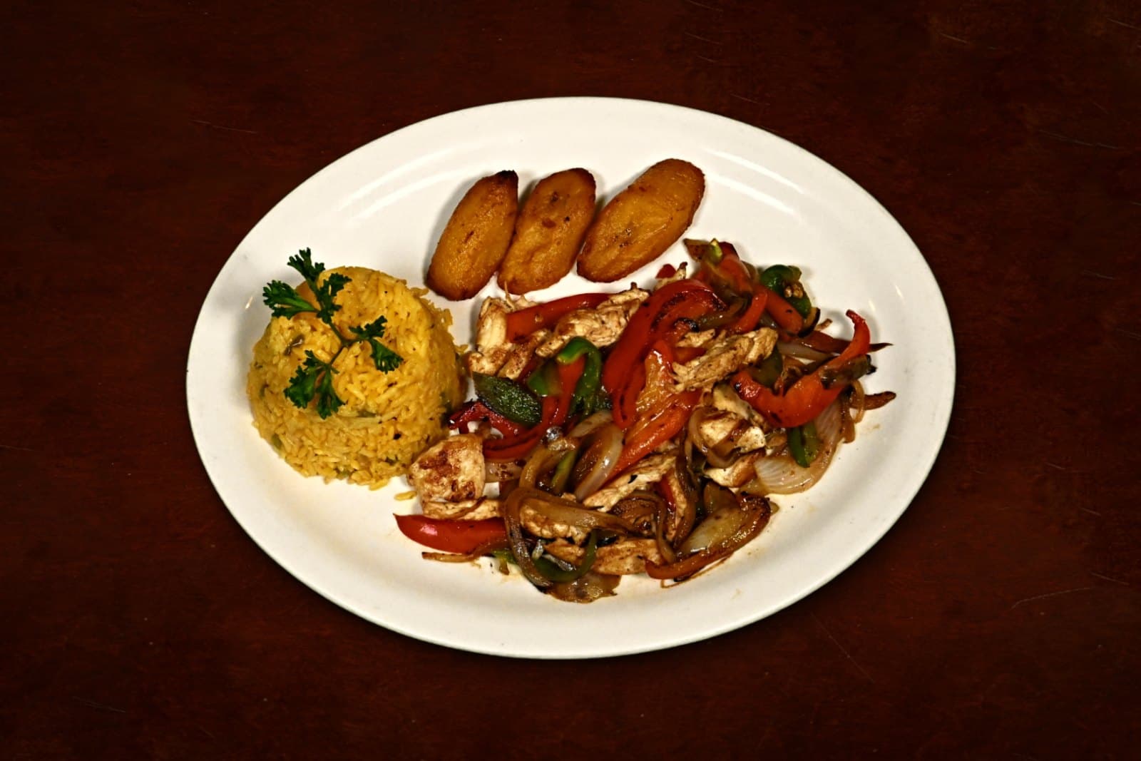 Pollo a la Juliana: sautéed with onions & peppers, yellow rice, maduros, plated on a dark wood table