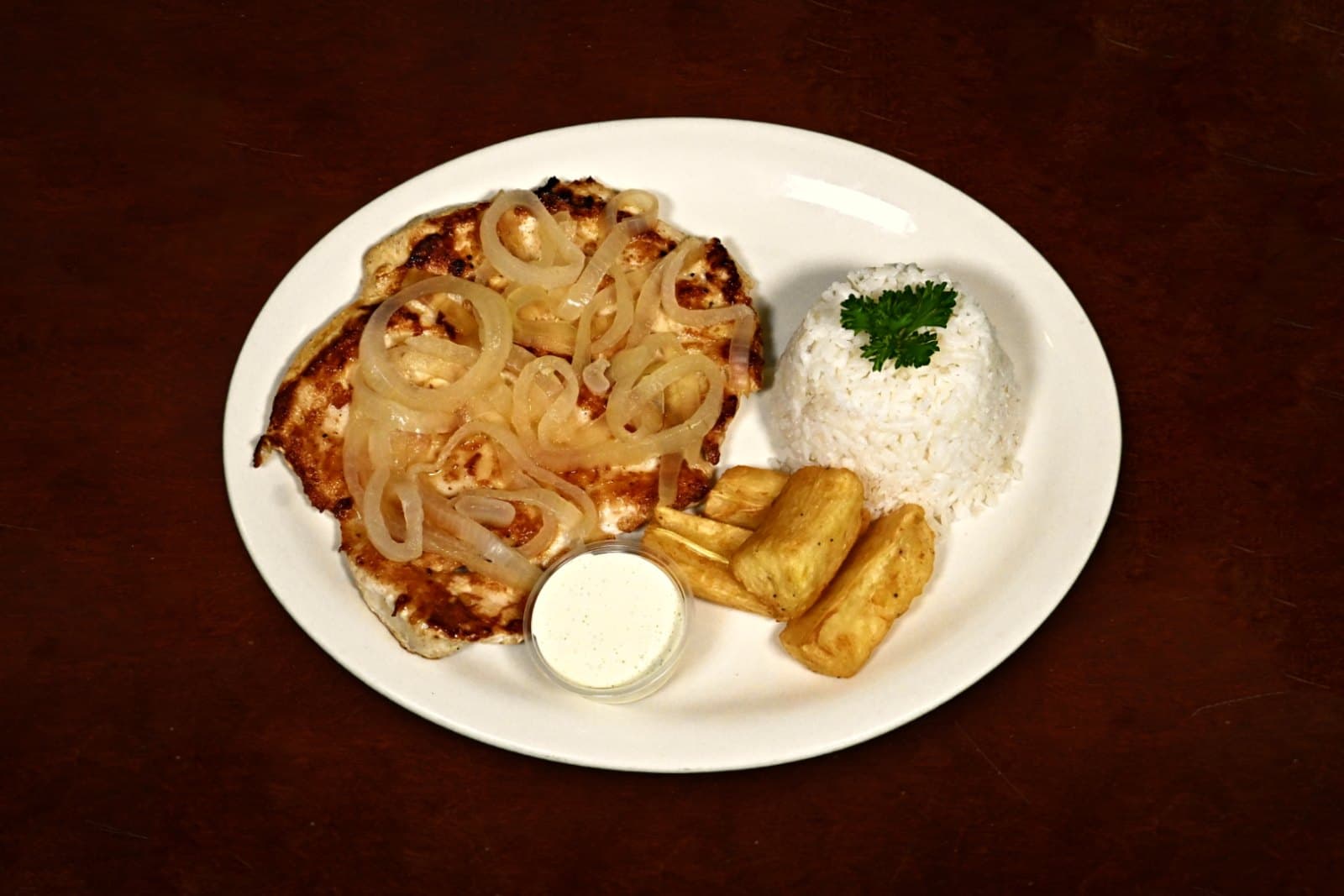 Bistec de Pollo: sautéed onions, white rice, yuca frita, plated on a dark wood table
