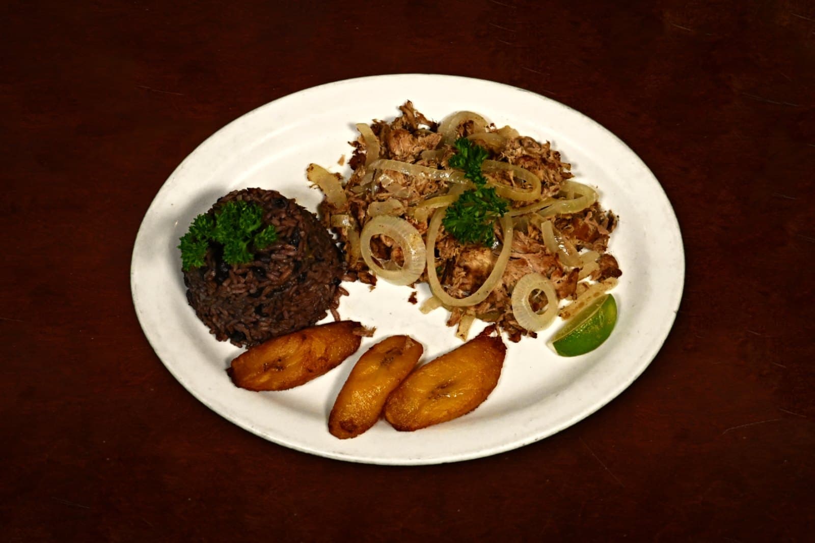 Vaca Frita: marinated flank steak, sautéed onions, moros & maduros, plated on a dark wood table