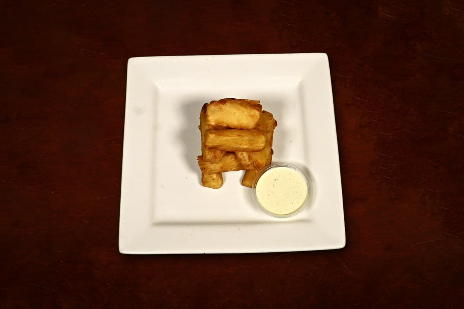 Yuca Frita: with cilantro sauce, plated on a dark wood table