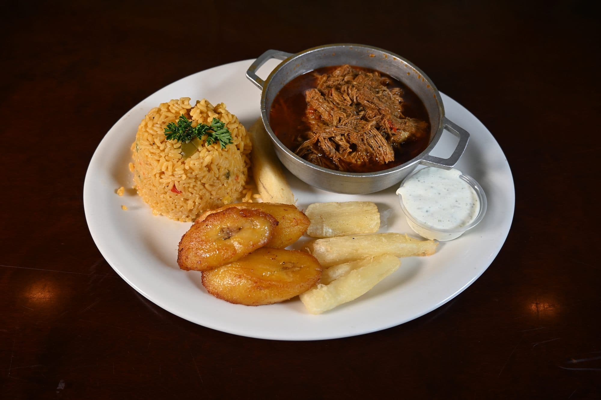 Ropa Vieja — shredded flank steak in creole sauce, served in a caldero with yellow rice, maduros and yuca